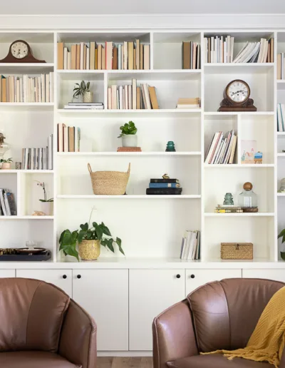 Two brown leather chairs in front of a white bookcase.
